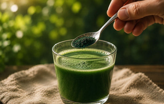 Close-up of a hand adding a teaspoon of deep blue-green spirulina into a green smoothie